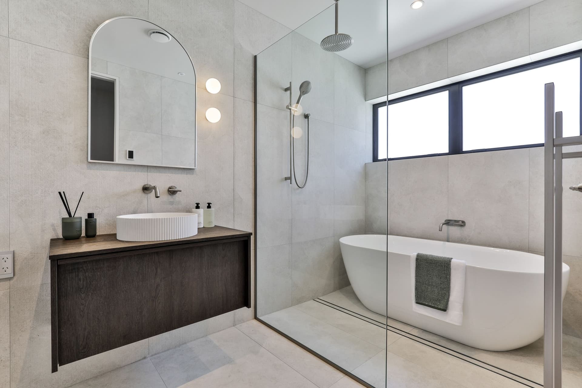 Wet room in pale large-format tile with a freestanding bath behind a glass screen