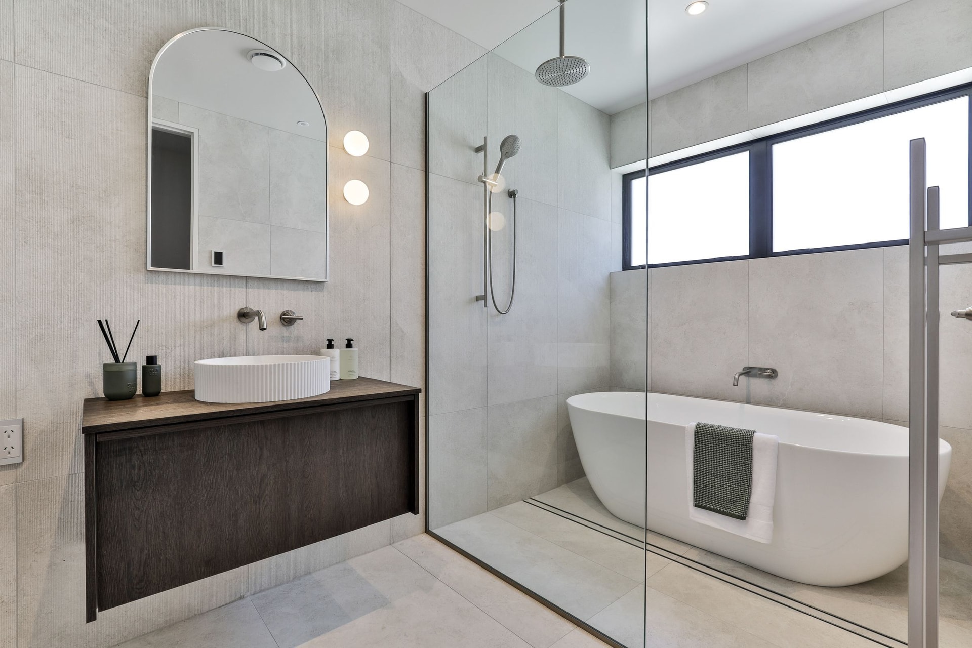 Wet room in pale large-format tile with a freestanding bath behind a glass screen