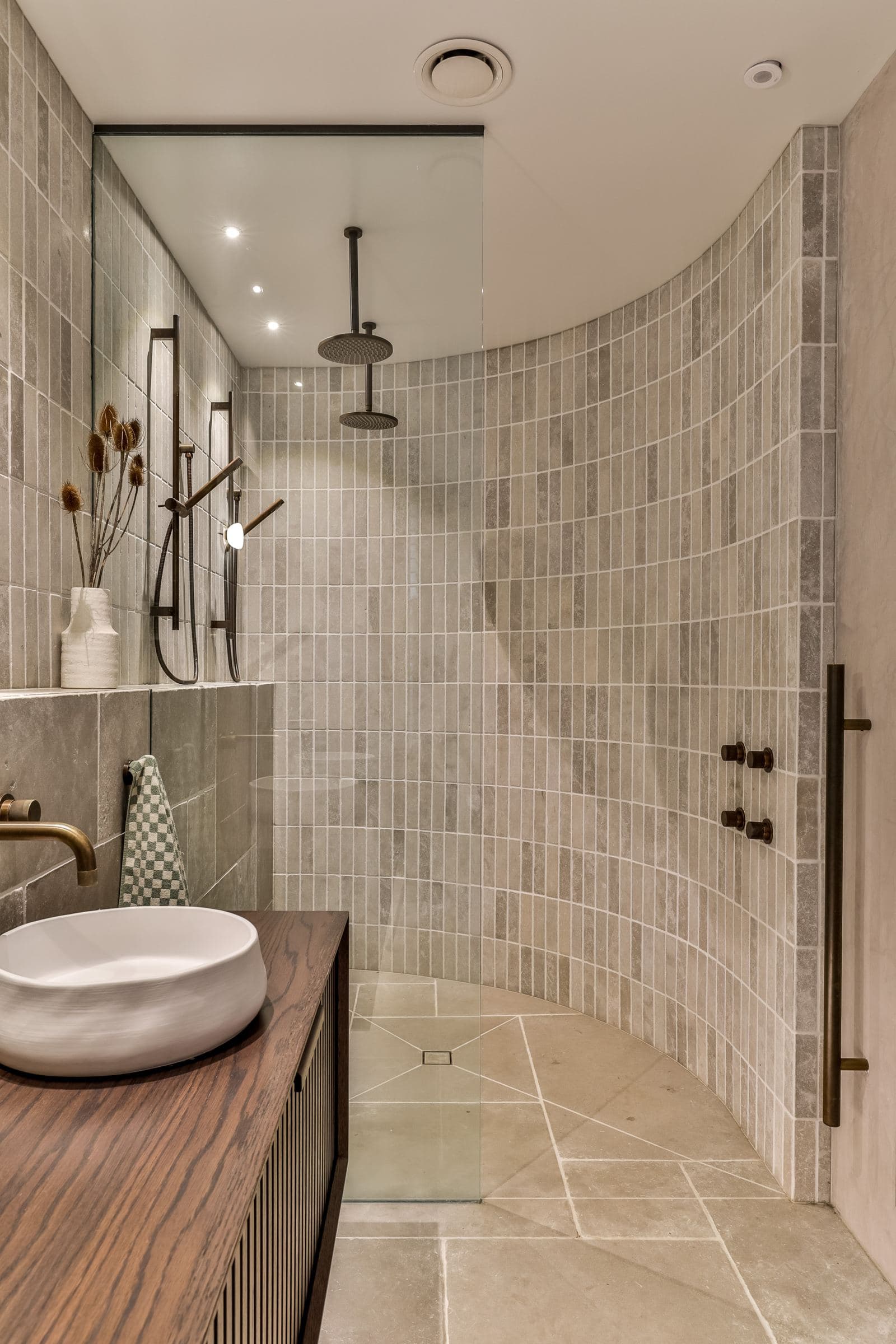 Curved shower wall in grey stone finger tile, with two ceiling showers and a cut-stone floor