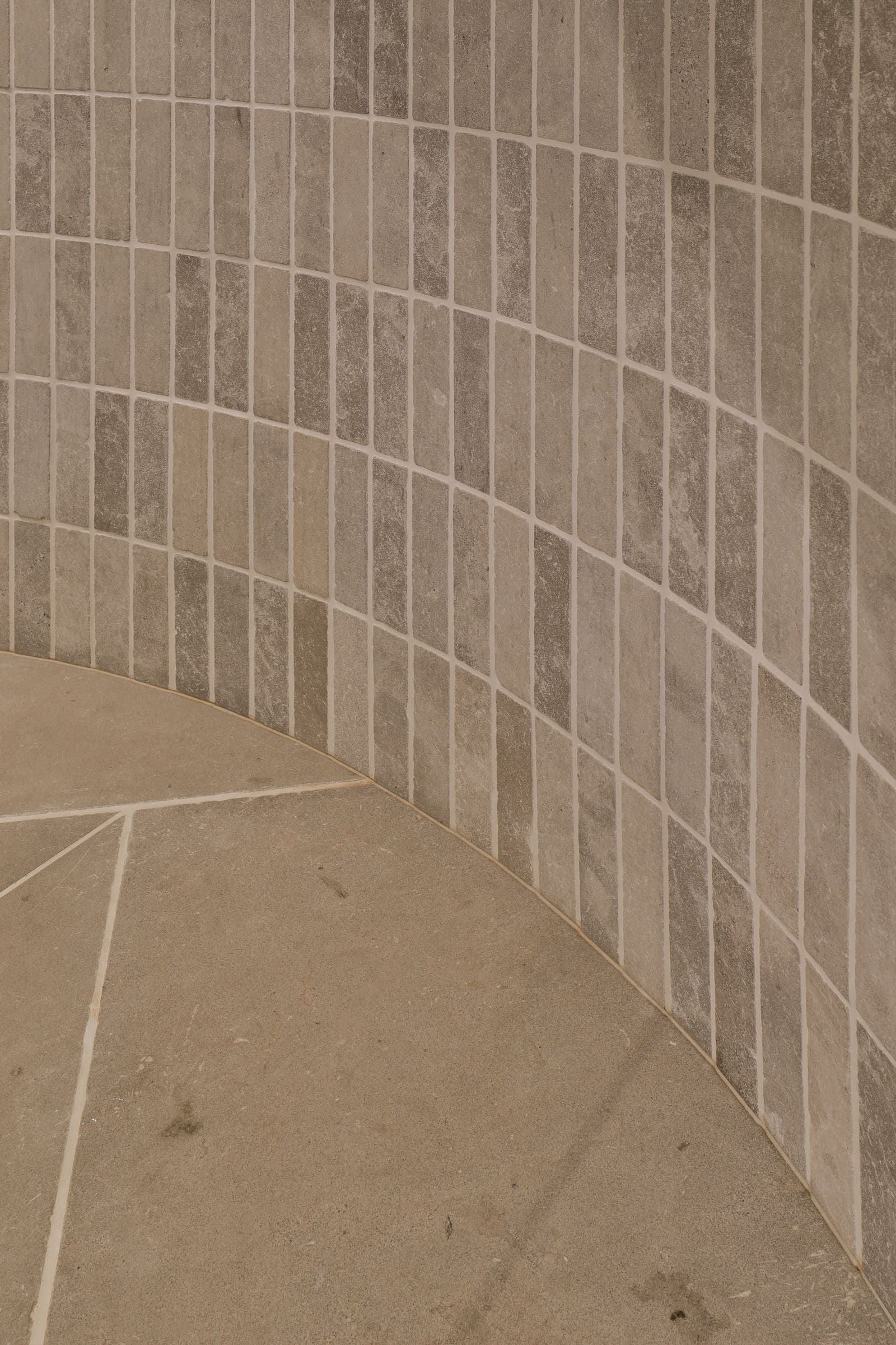Close-up where the curved finger-tile wall meets the random-cut stone floor