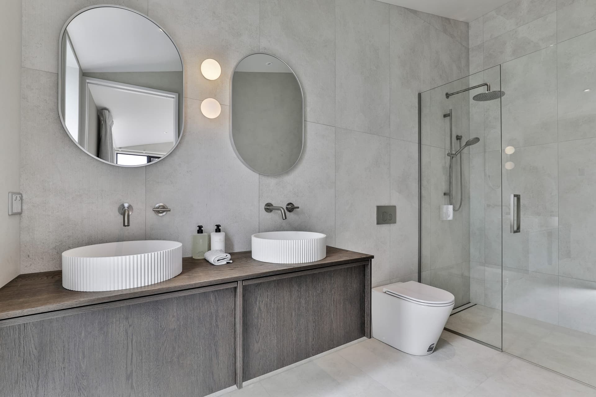 Ensuite with a double vanity, two round basins and oval mirrors on pale large-format tile