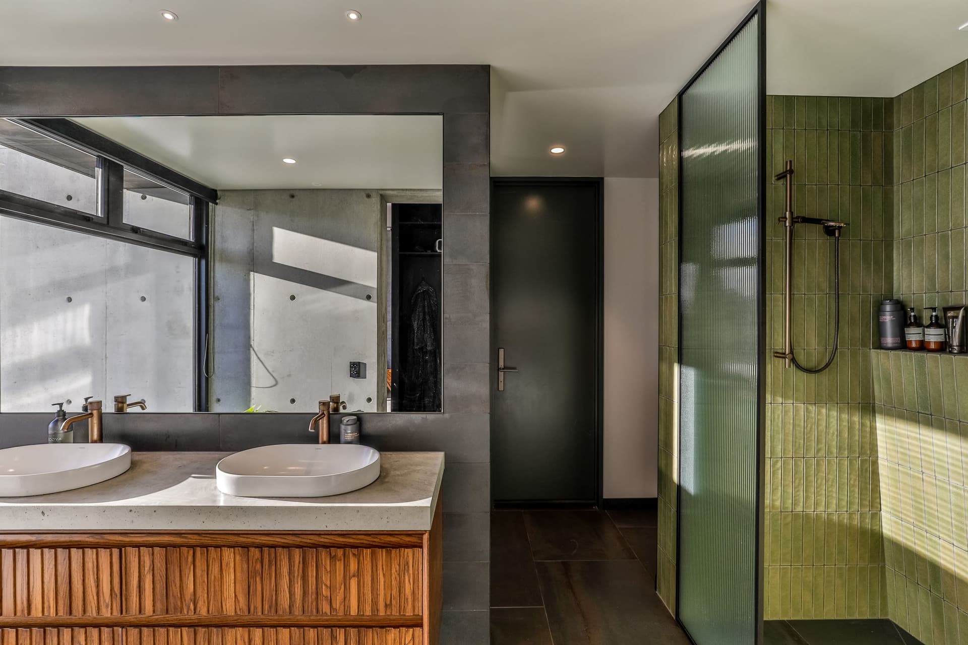 Ensuite with concrete benchtop, oak vanity and a shower in handmade green vertical tile behind reeded glass