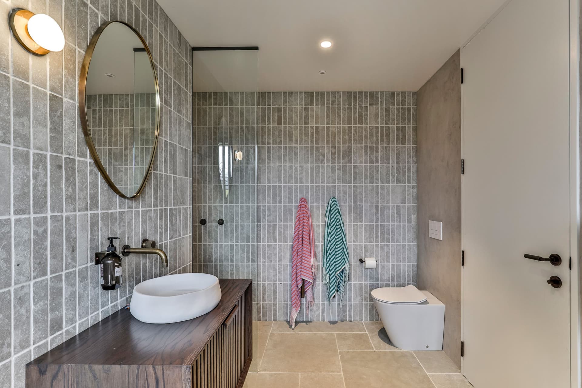 Second bathroom with grey finger tile, an oval brass mirror and a stone floor