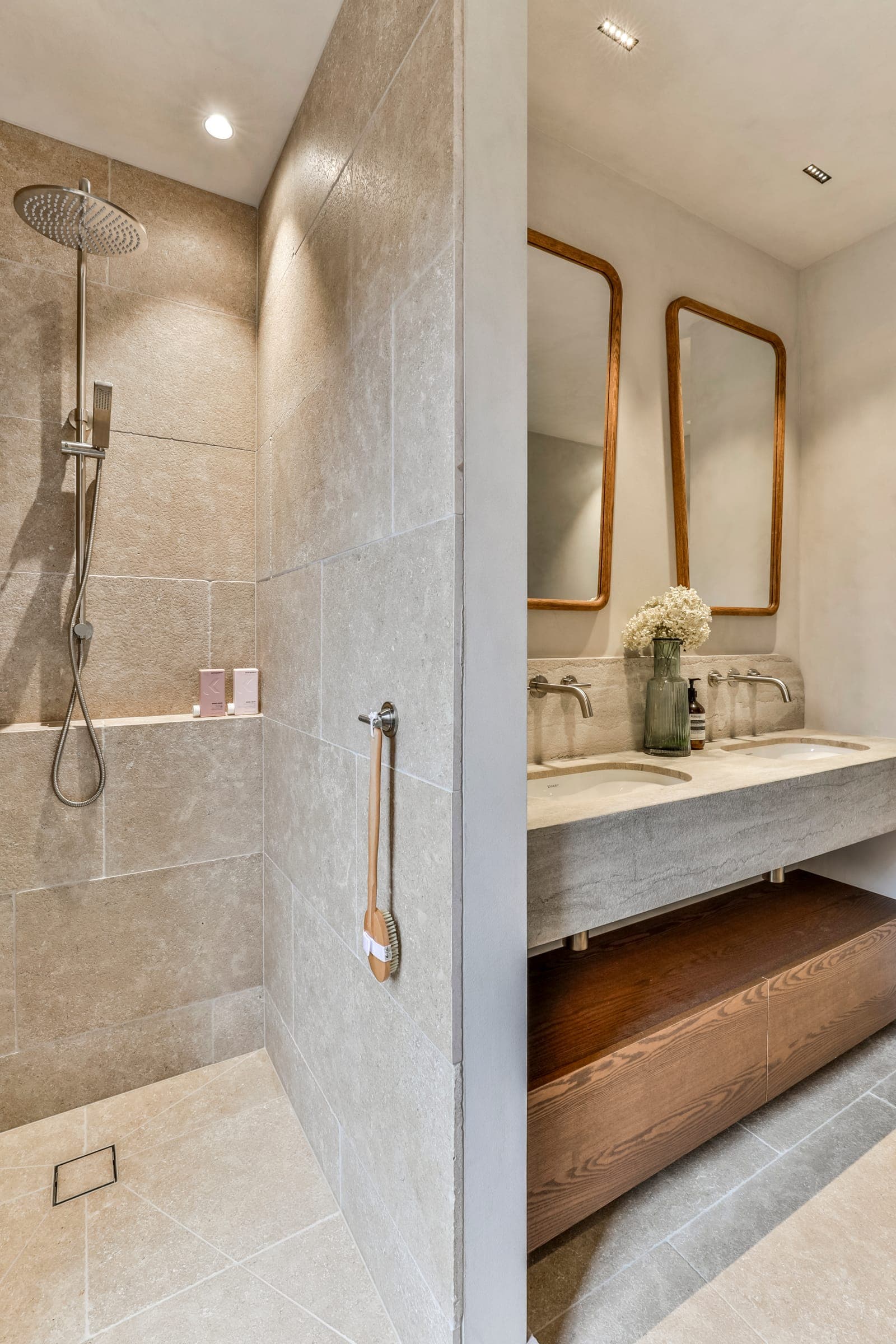 Limestone shower beside a stone vanity with two timber-framed mirrors