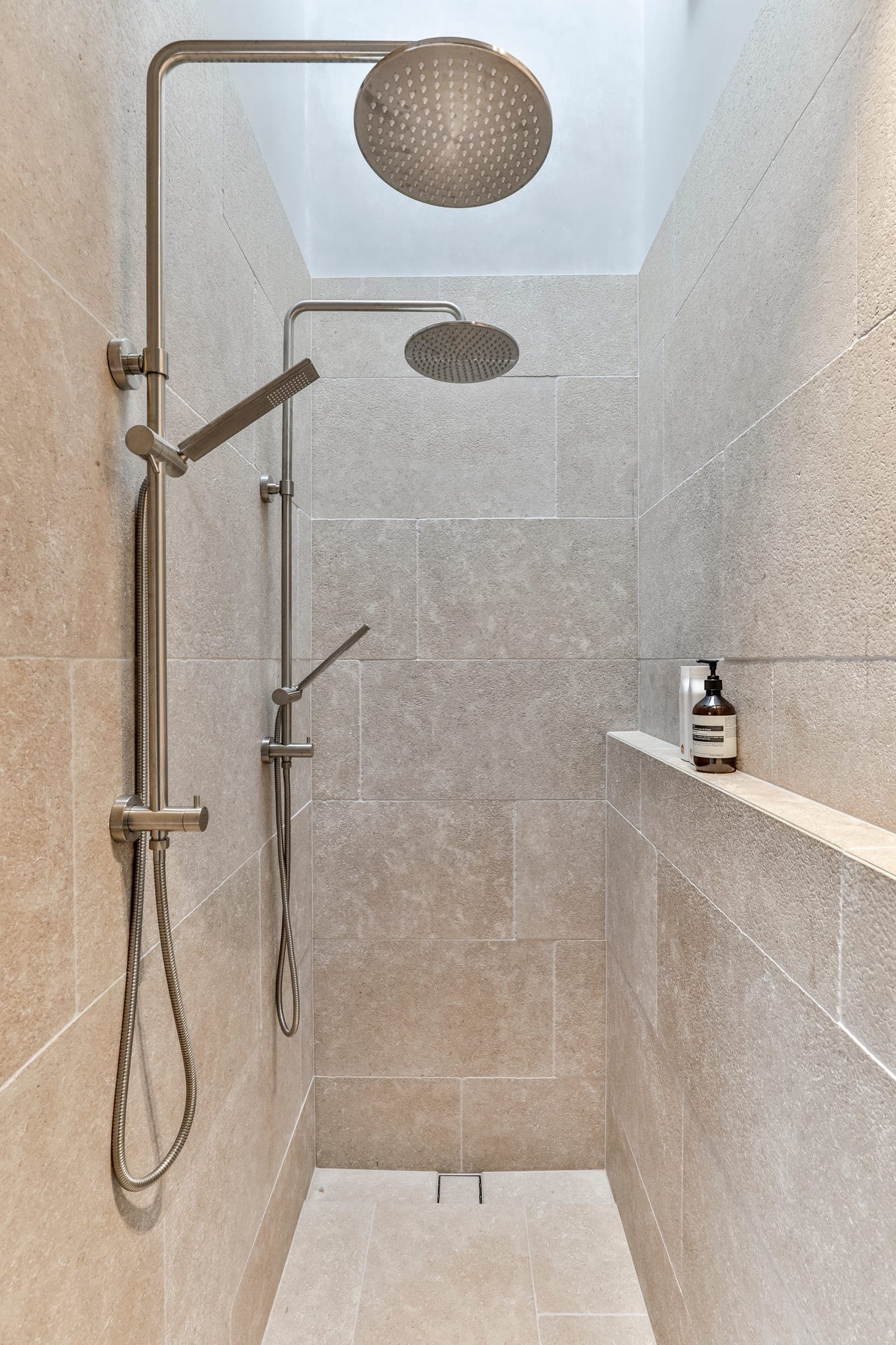 Walk-in shower in honed limestone with two brass shower rails