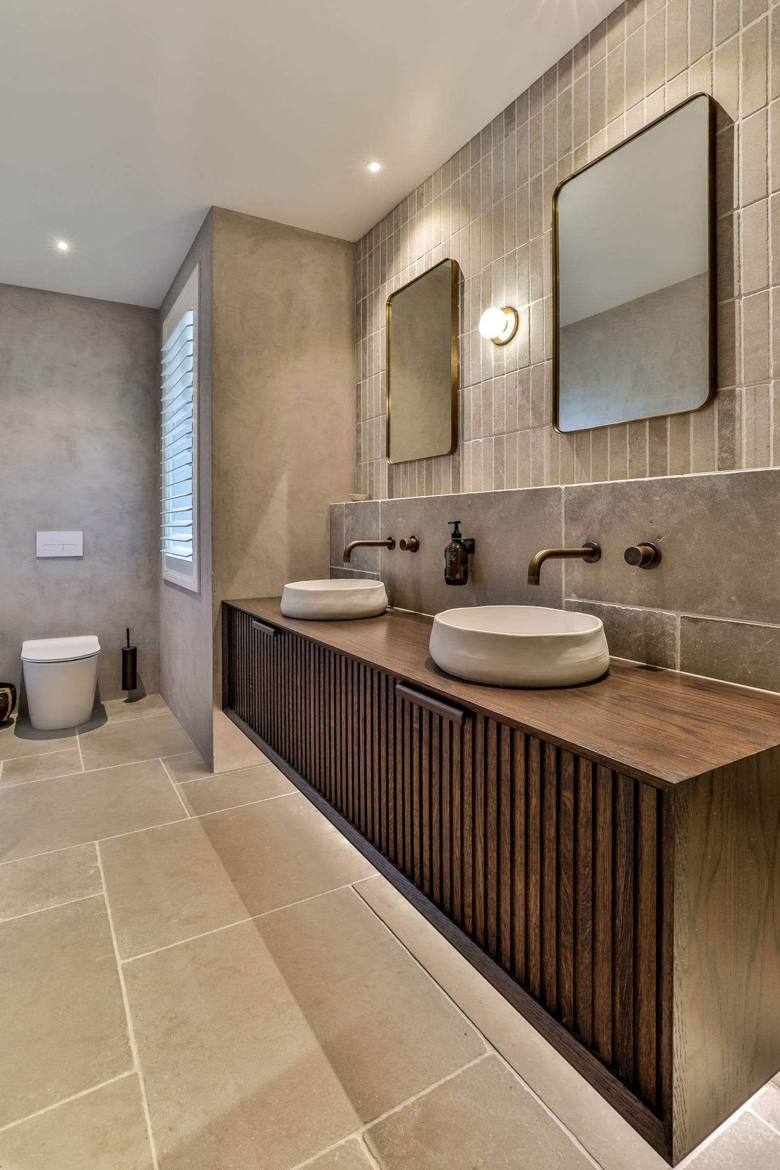 Large stone floor tiles running under a fluted oak vanity to the toilet wall