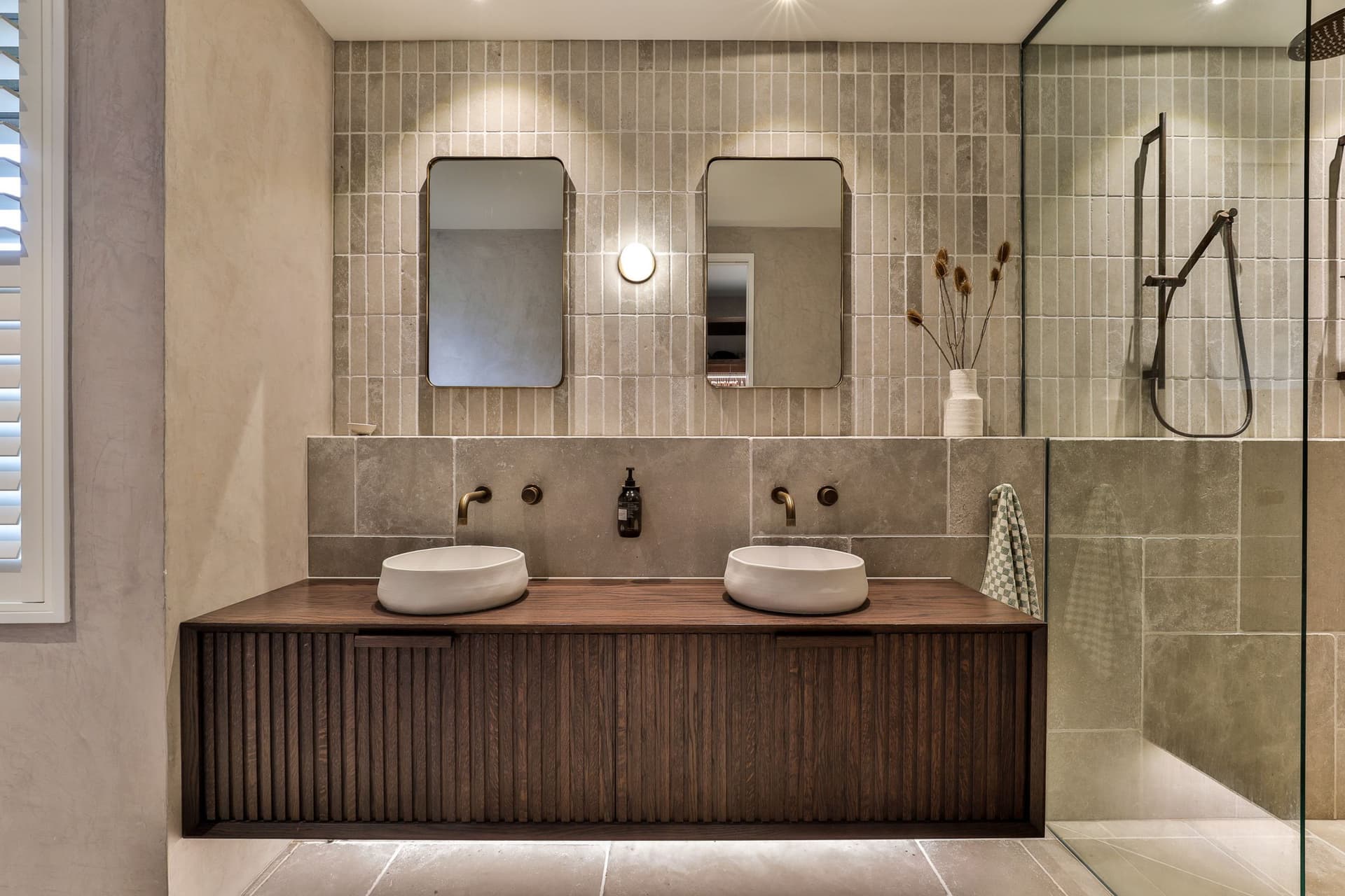Double vanity in dark fluted oak below two brass mirrors on stone finger tile
