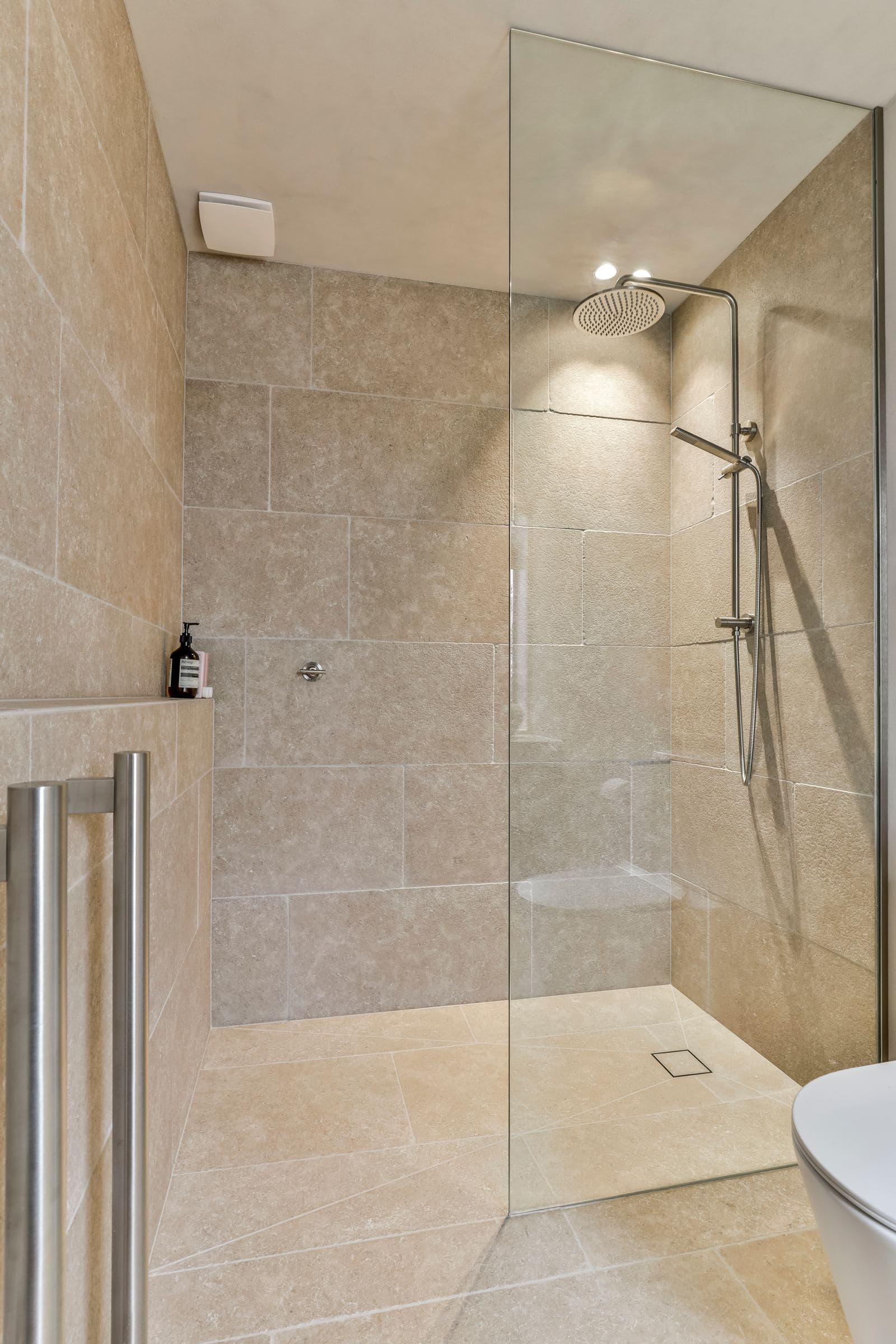 Walk-in shower lined in large honed limestone with a random-cut stone floor