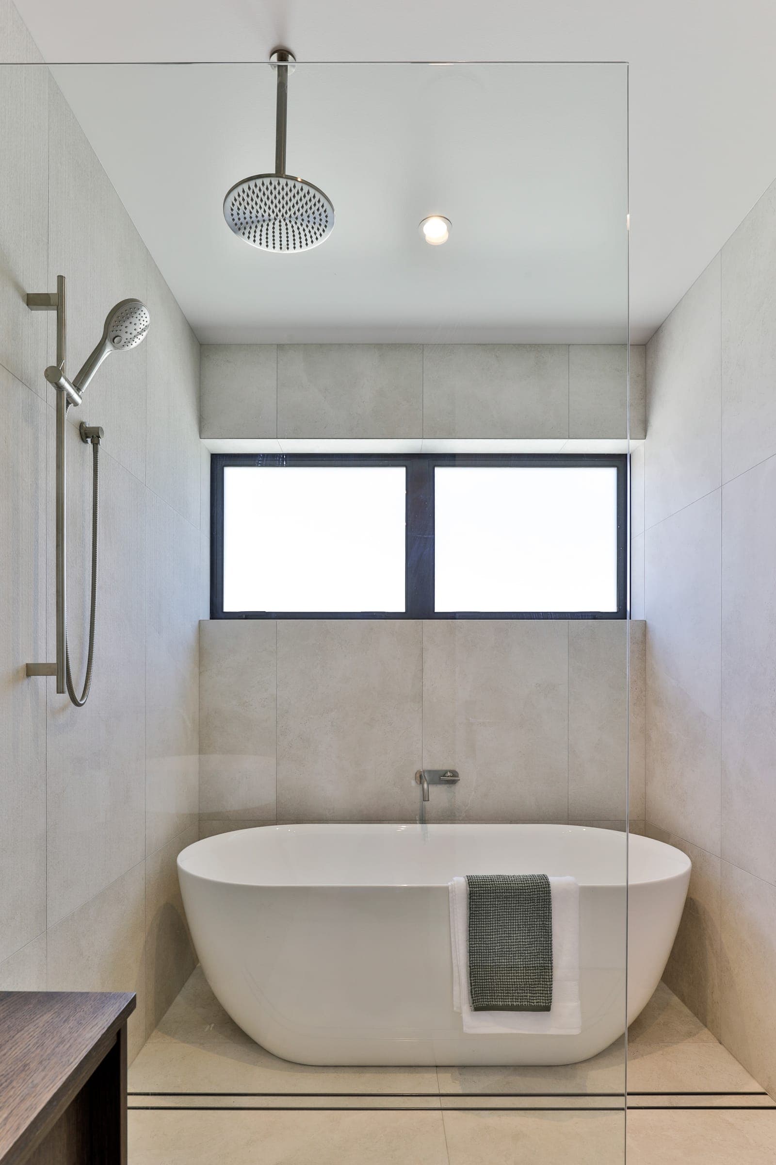Freestanding bath inside a pale tiled wet room, ceiling shower above